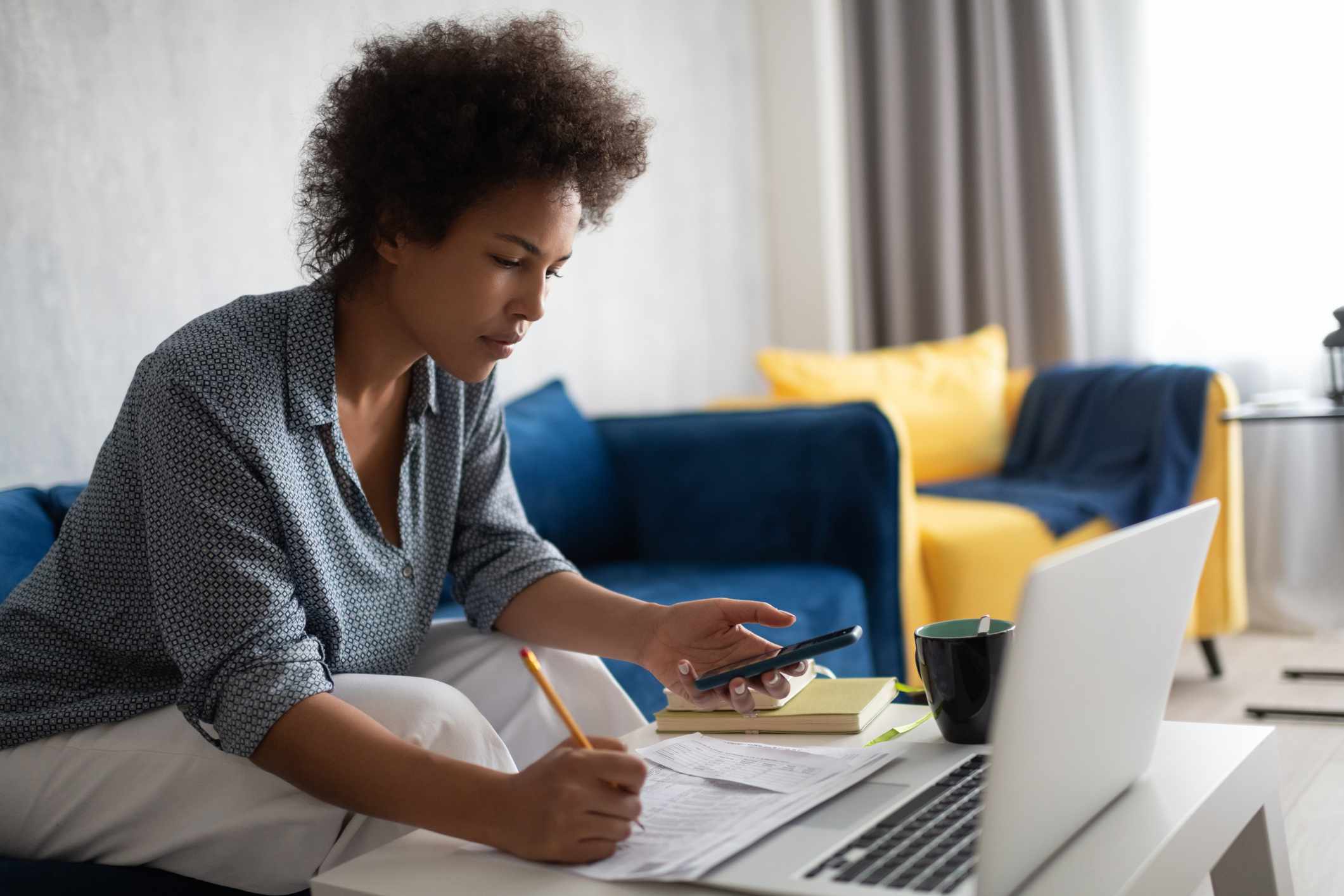 African American female using smartphone with a laptop and papers