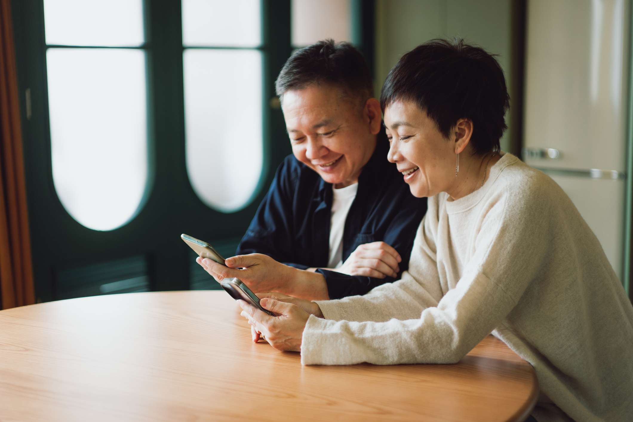 A couple sits at a table looking at their devices.