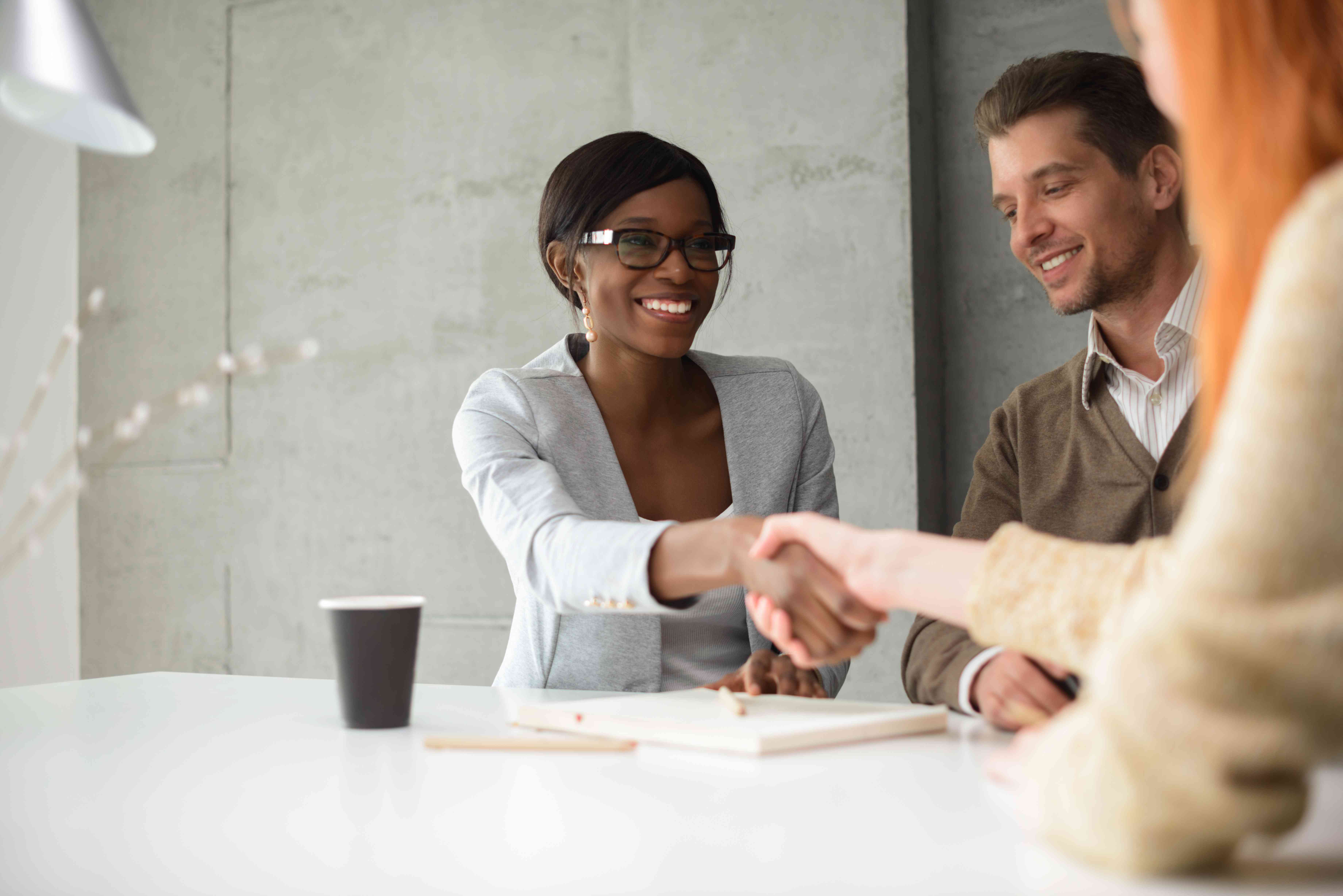 Two people shake hands in an office setting.