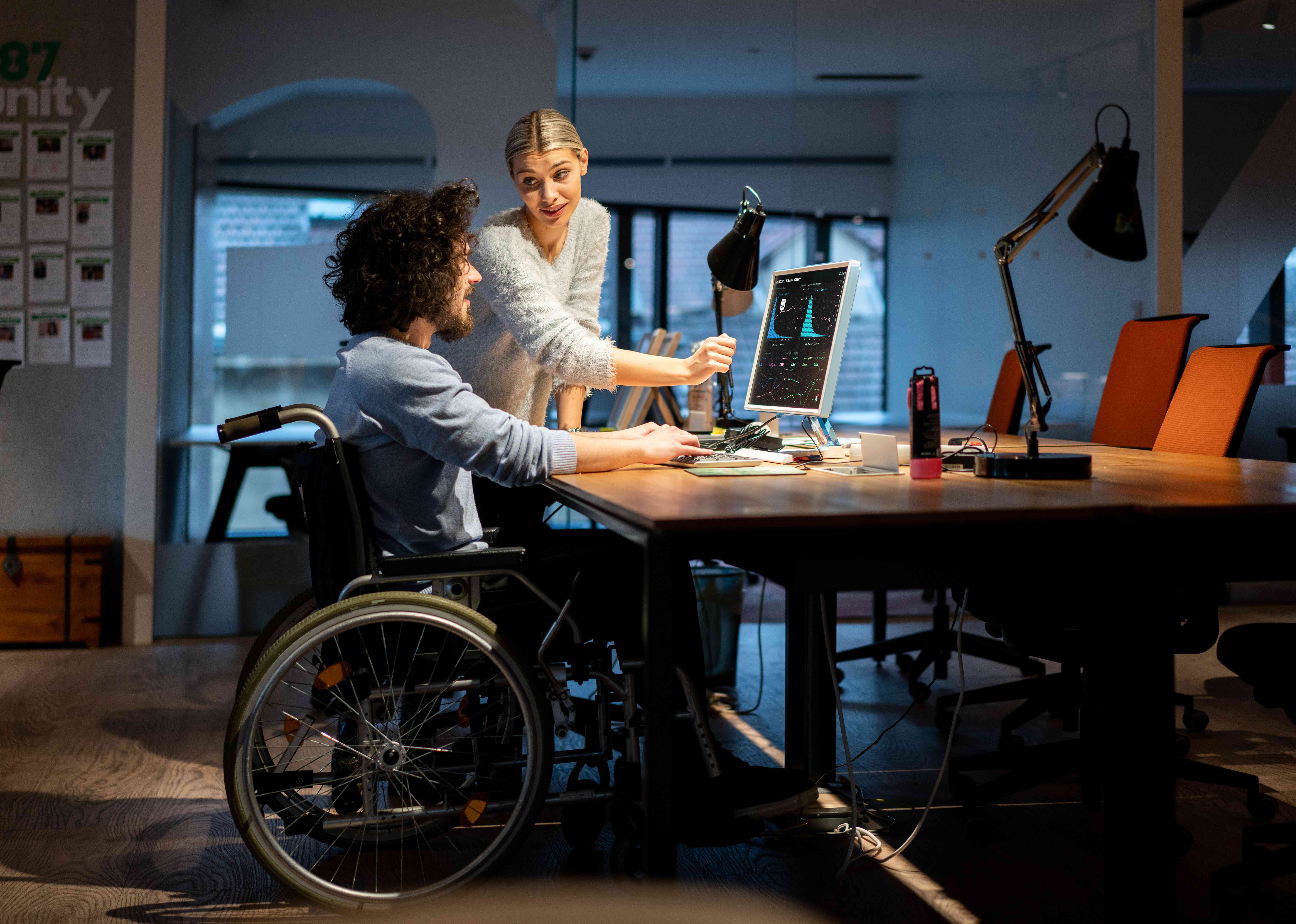 A man and a woman sit at a desk looking at a computer screen with charts and graphs on it