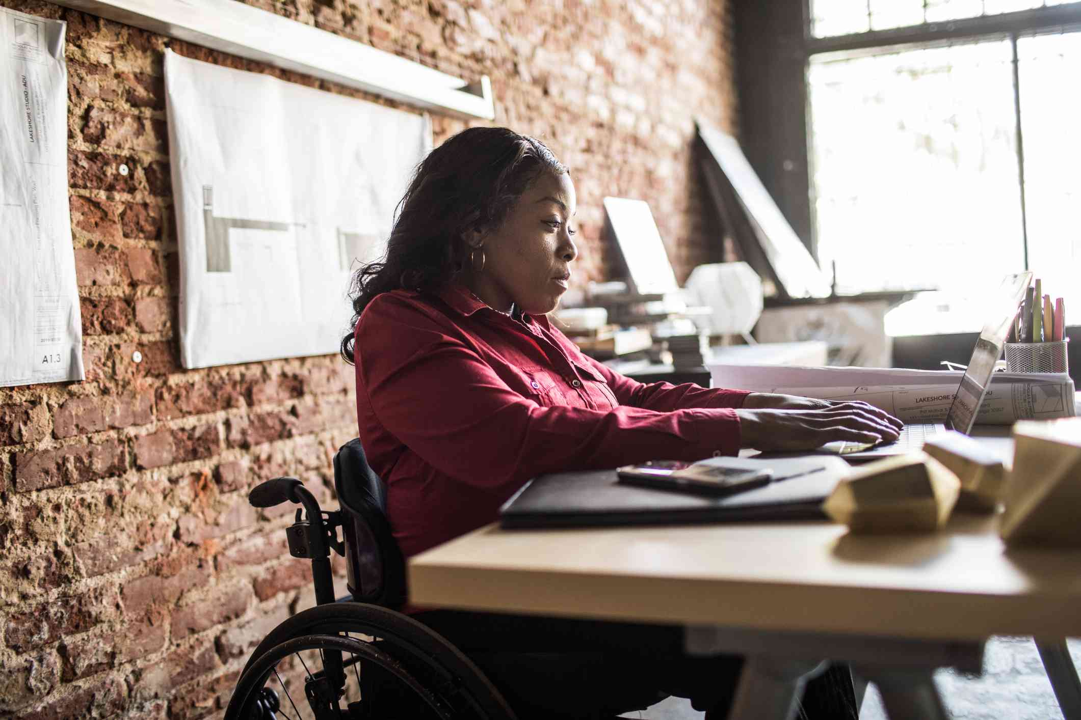 A woman seated in a wheelchair at a desk working on a laptop.