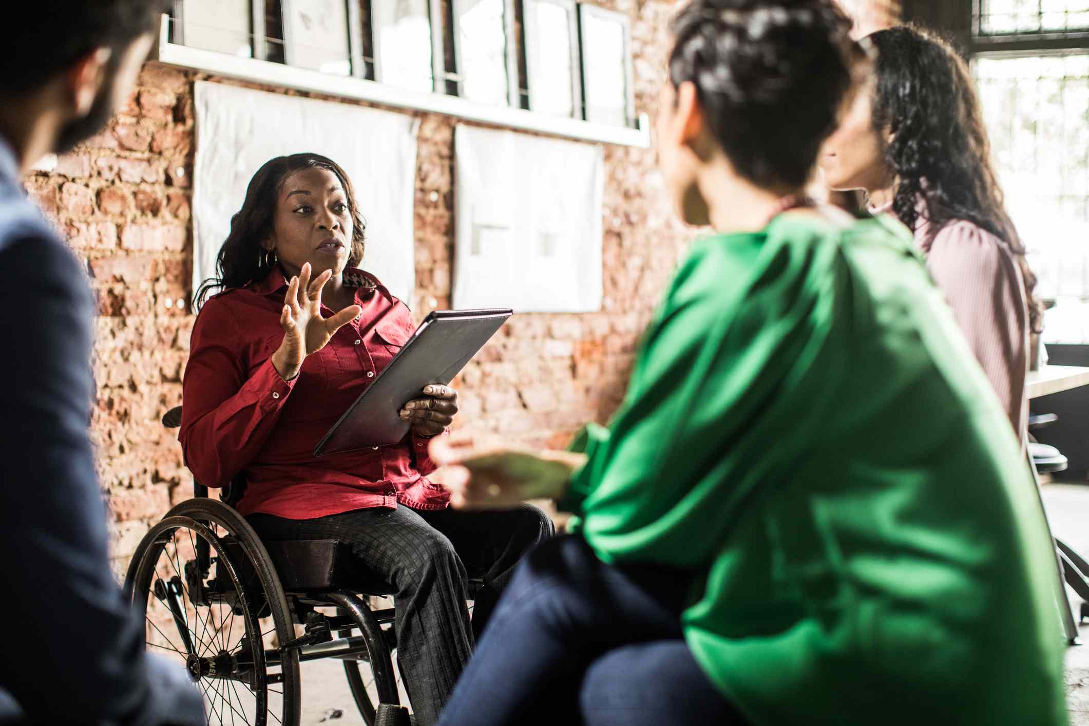 A group of people sitting and facing a person in wheelchair who is leading a work meeting