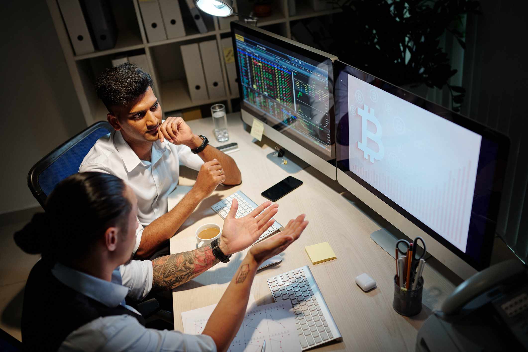 Two People Discuss Crypto Trading While Looking at Computer Screens