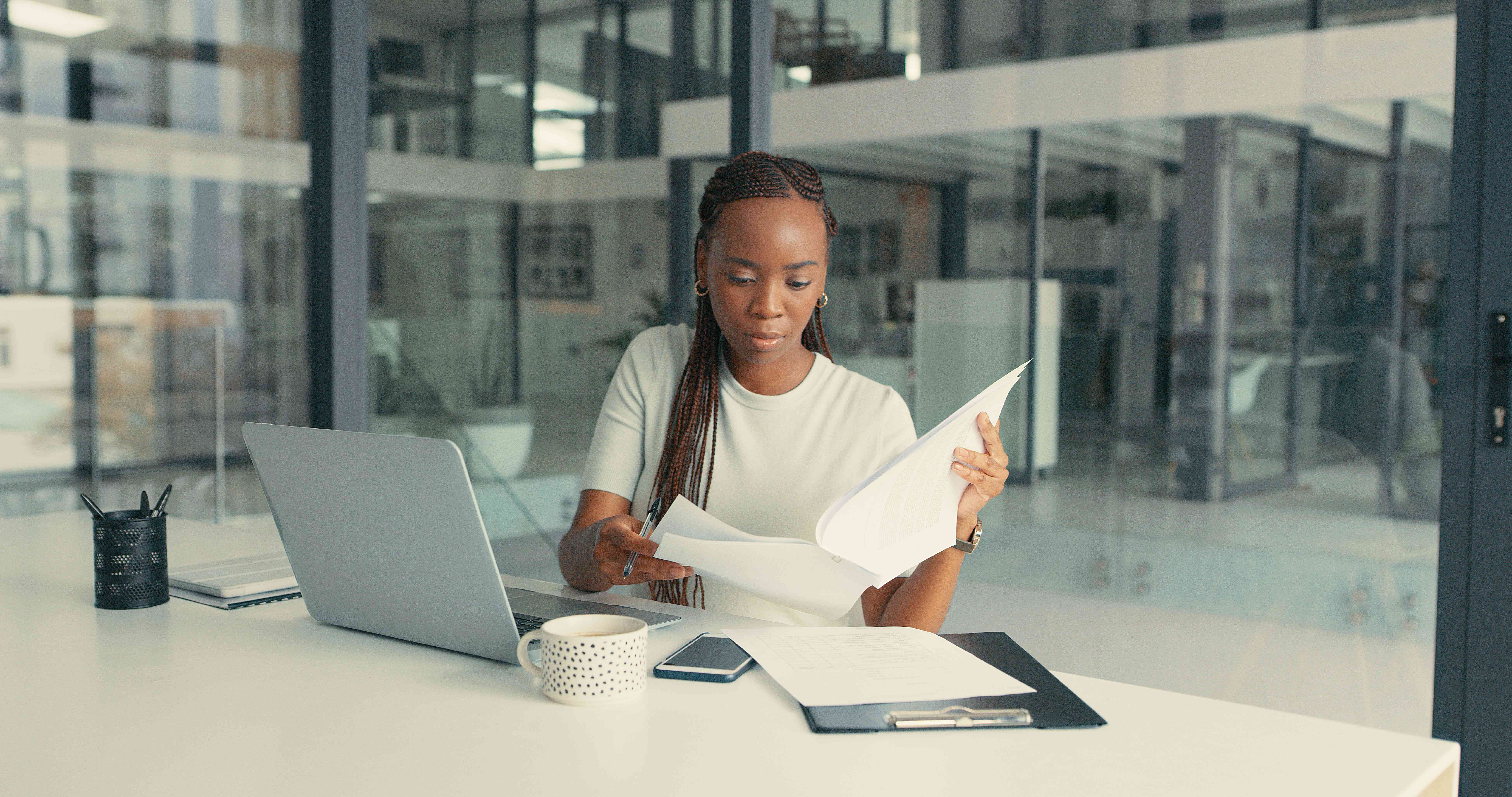 Woman reading through paperwork with a laptop at a desk