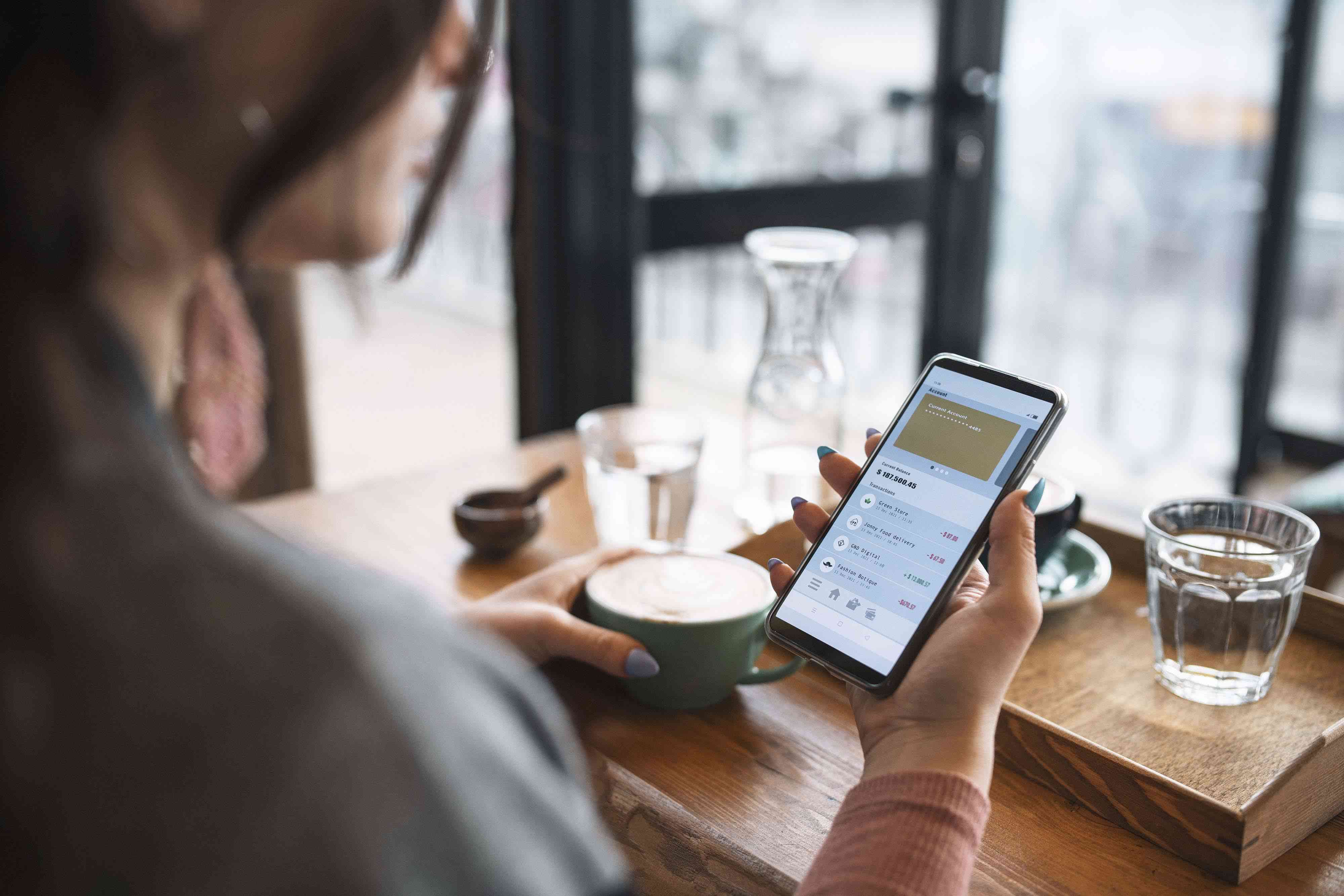 young woman managing savings bank account on smartphone at cafe