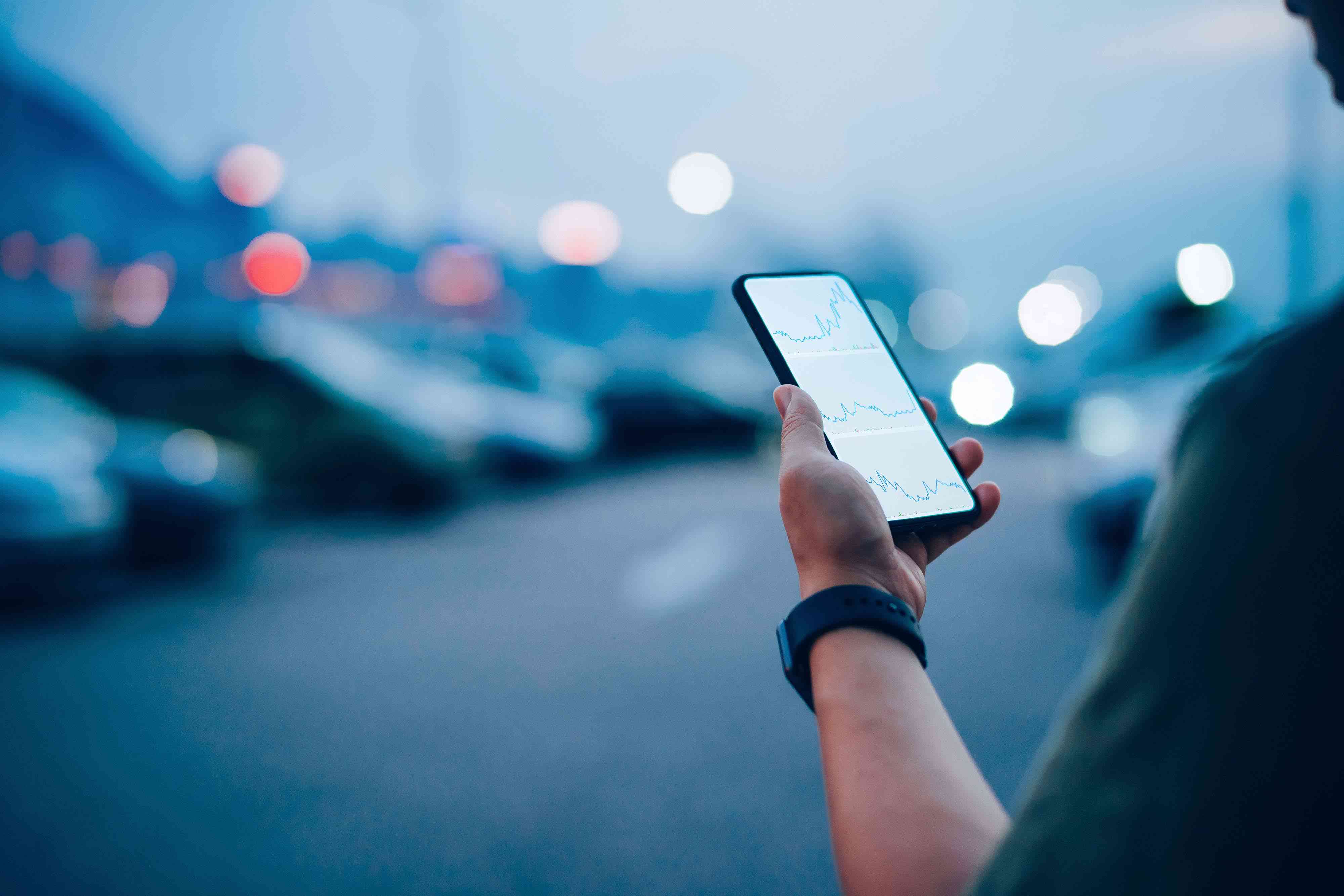 Over the shoulder view of businessman checking financial trading data on smartphone while walking to his car