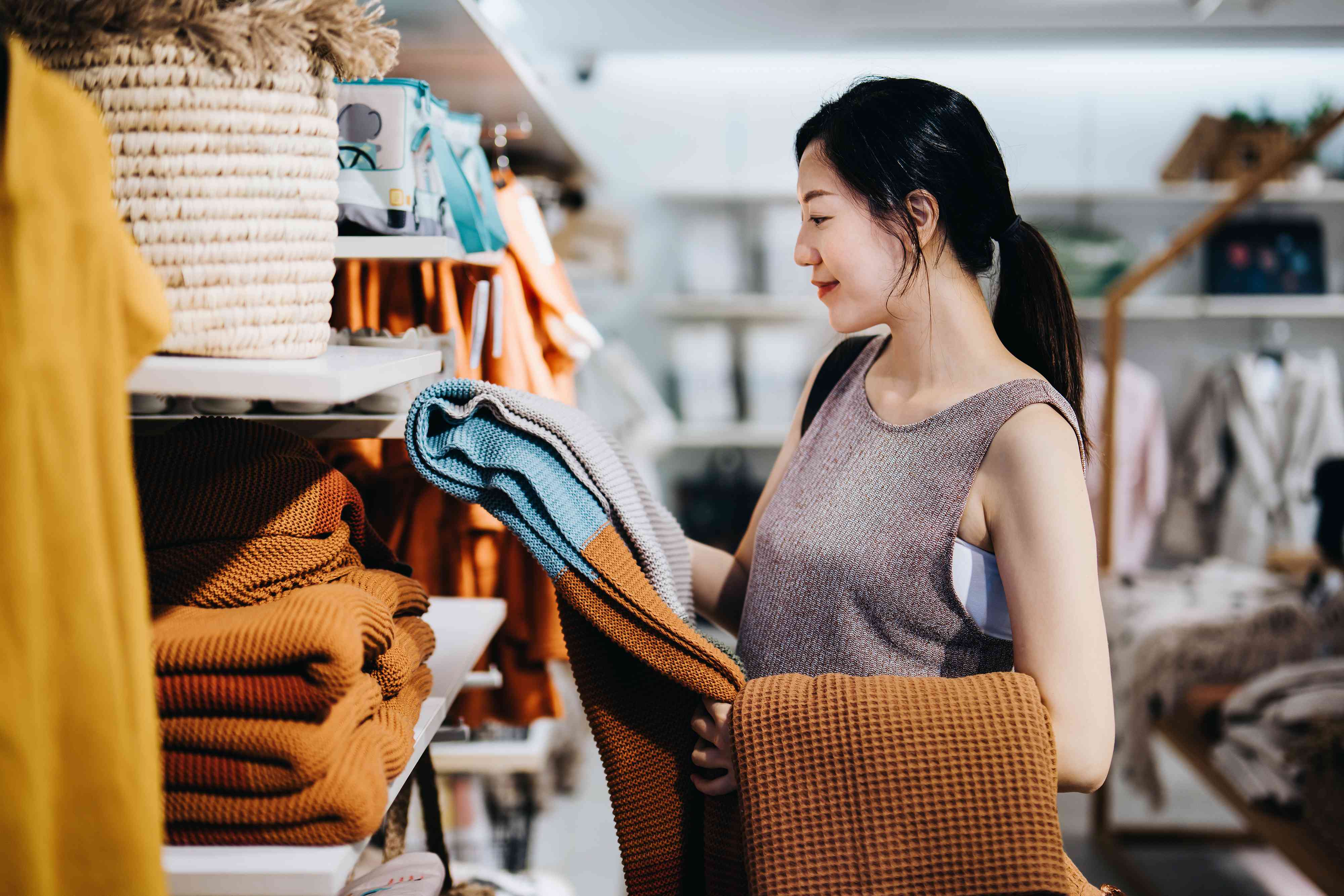 woman shopping for home decor and necessities in a homeware store, choosing for a blanket on a shelf