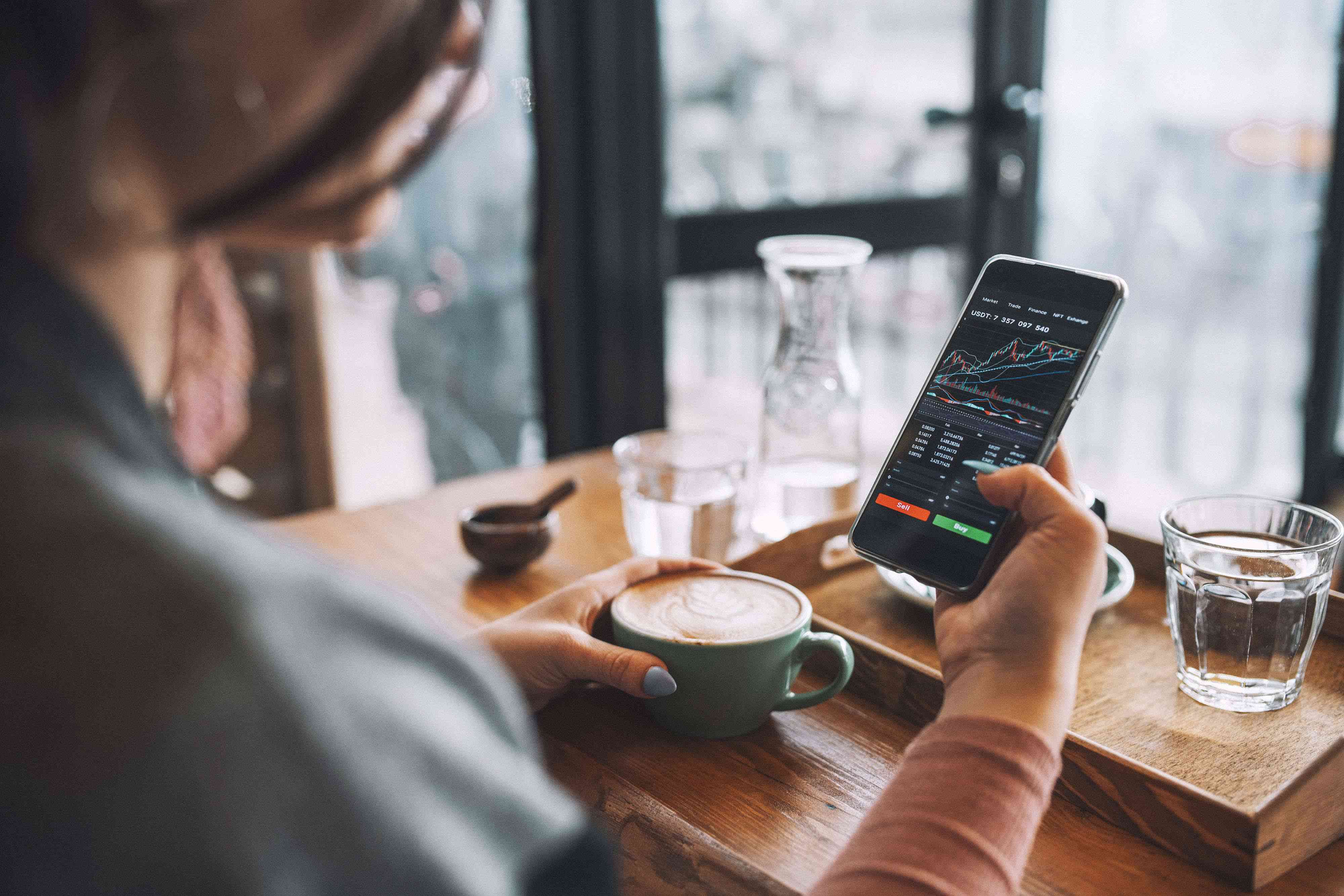 Woman using smartphone to trade fractional shares at a coffee shop