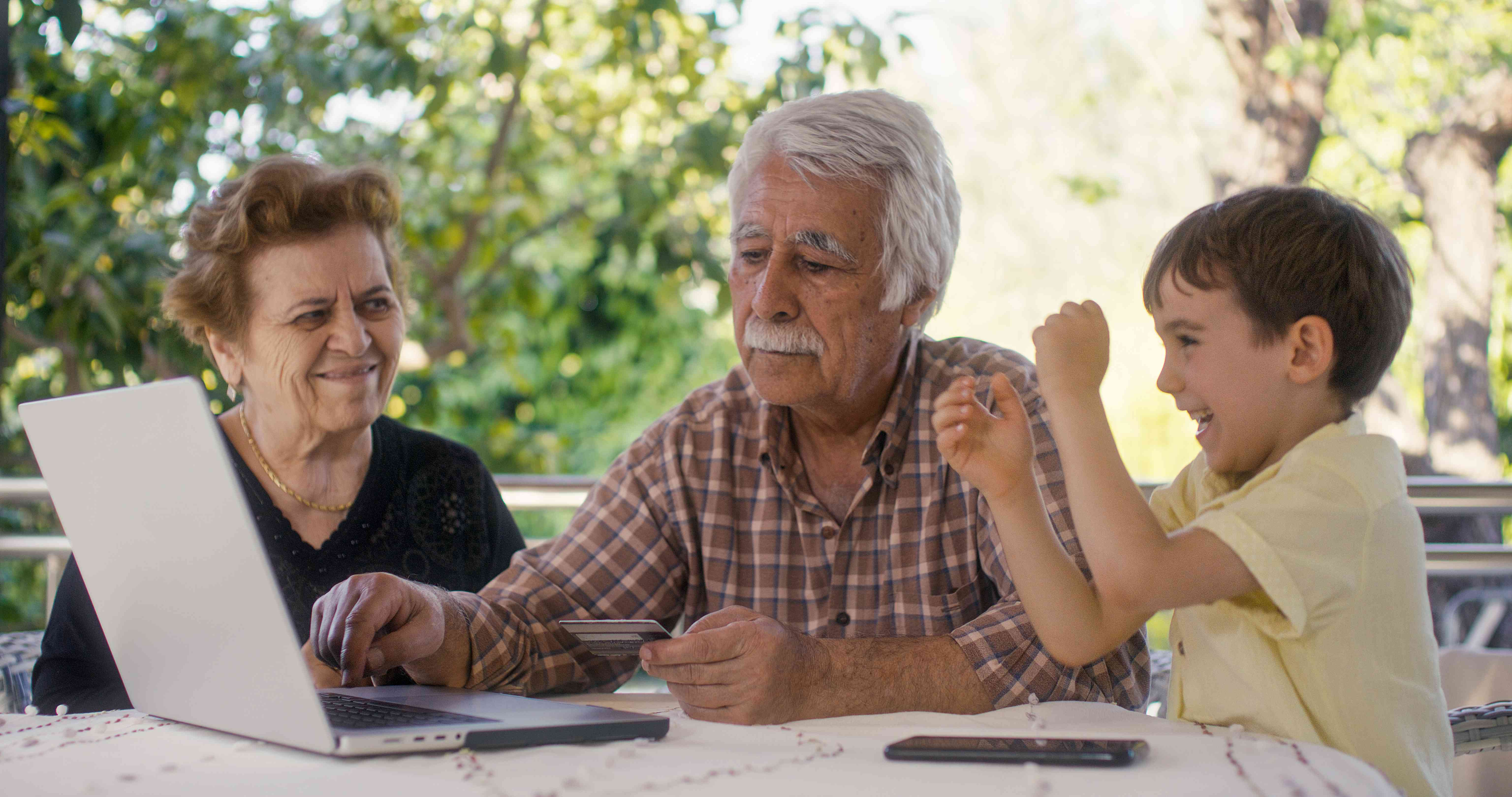 A young child celebrates as their grandparents use a laptop to show them the value of their savings bonds account.