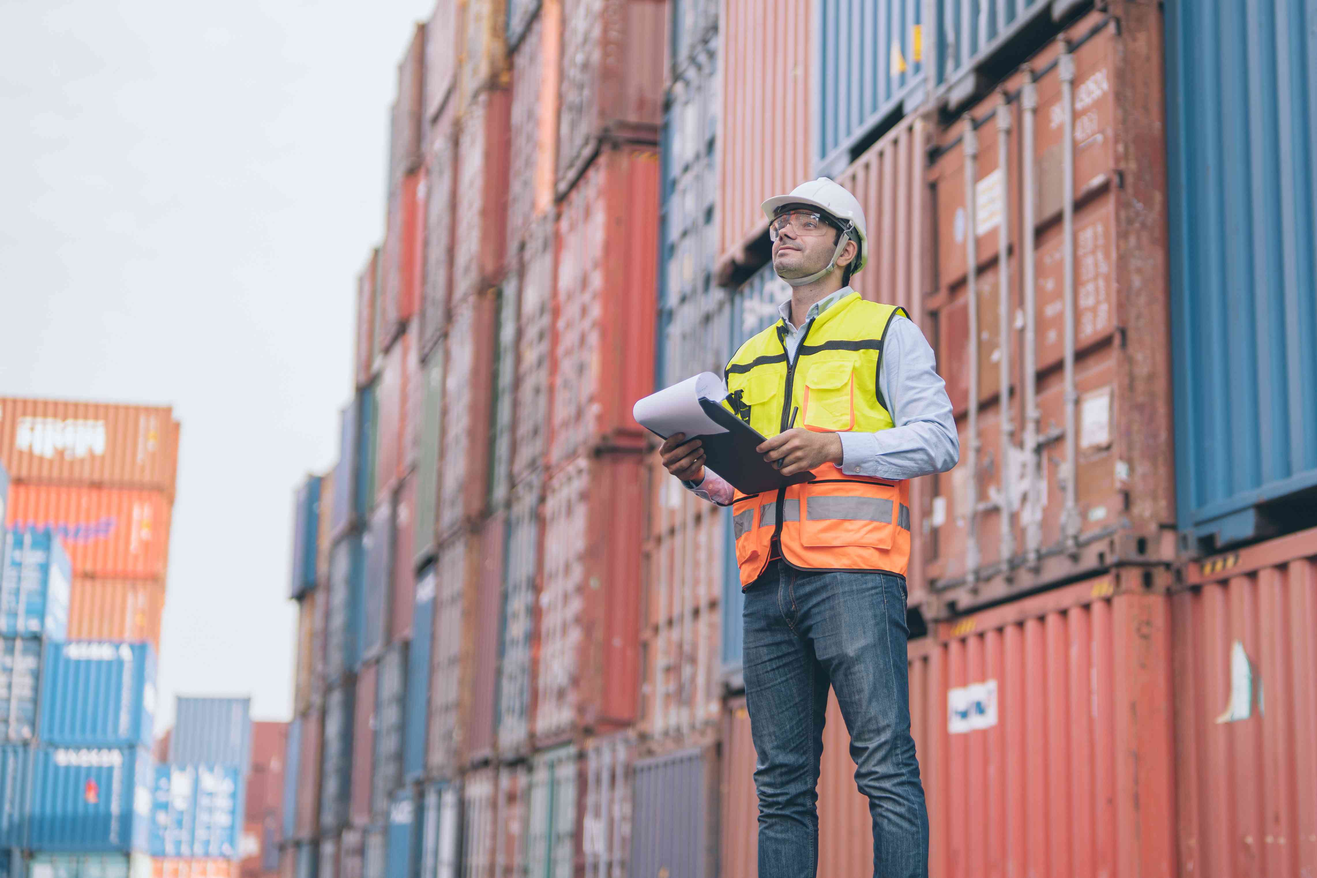 Dock worker stands in a shipyard flanked by shipping containers and examines a through bill of lading for transport.