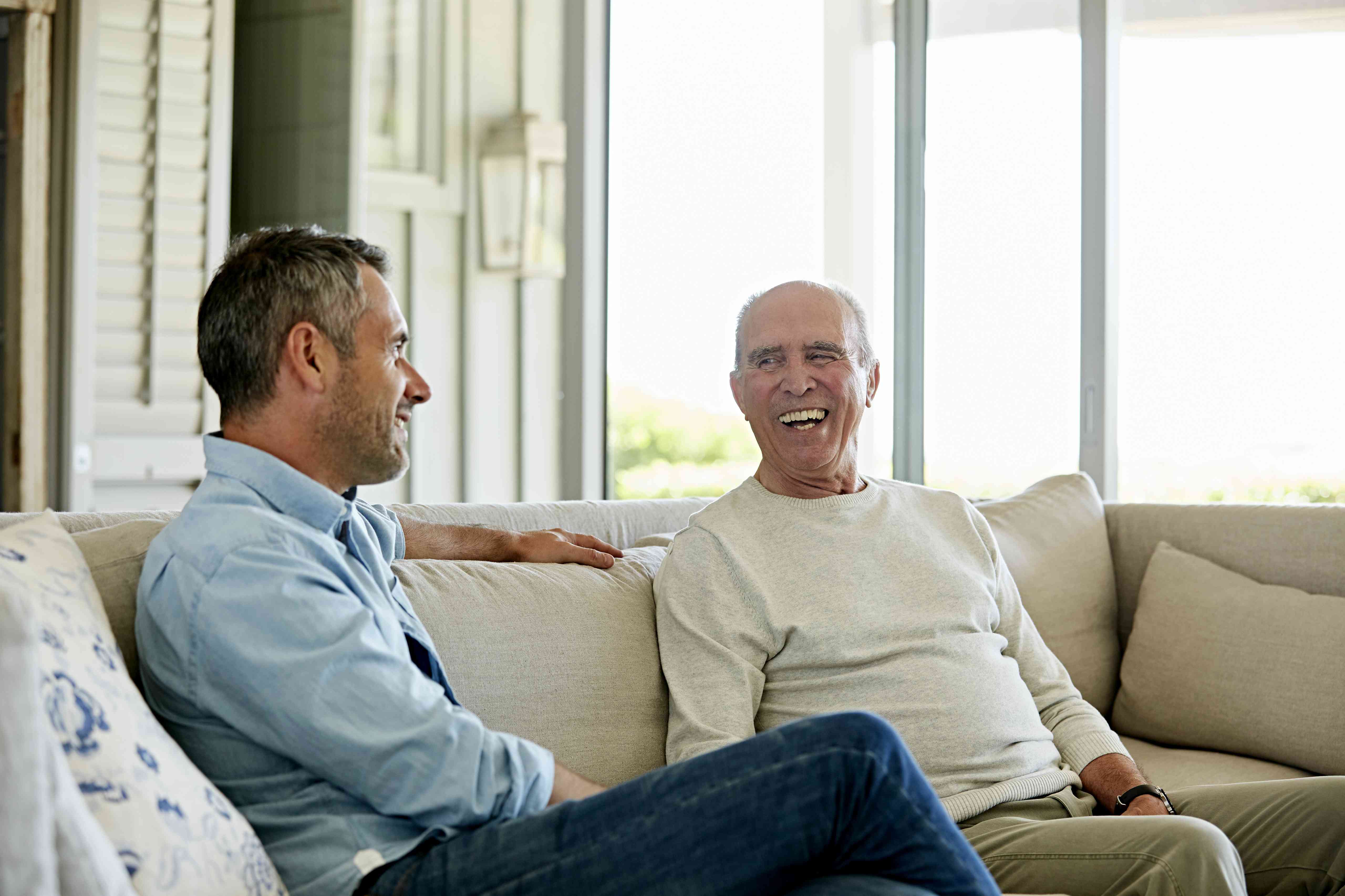 Two men have a conversation on a couch.