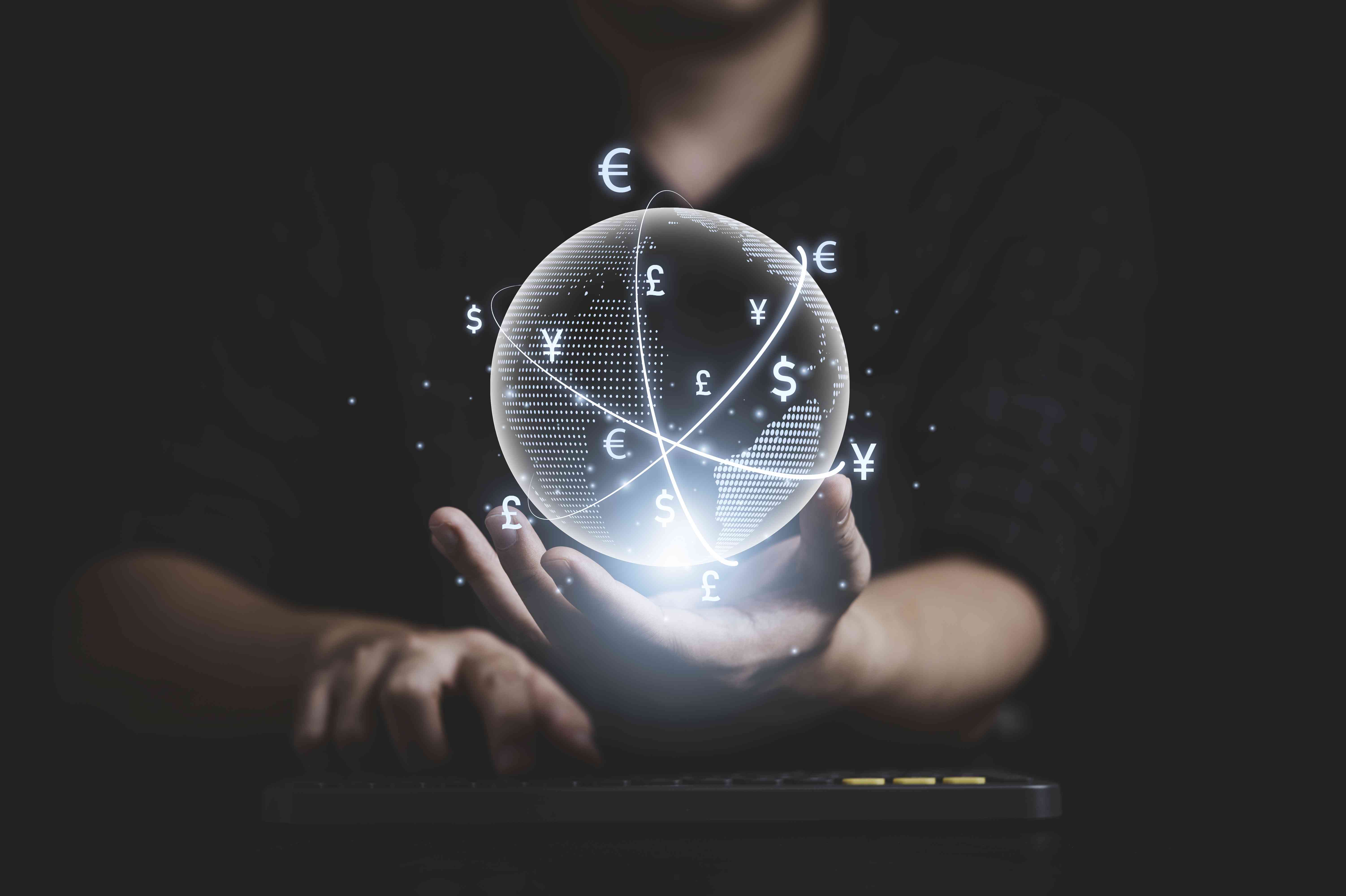 A banker holds a clear globe with international currencies circling it above a computer keyboard.