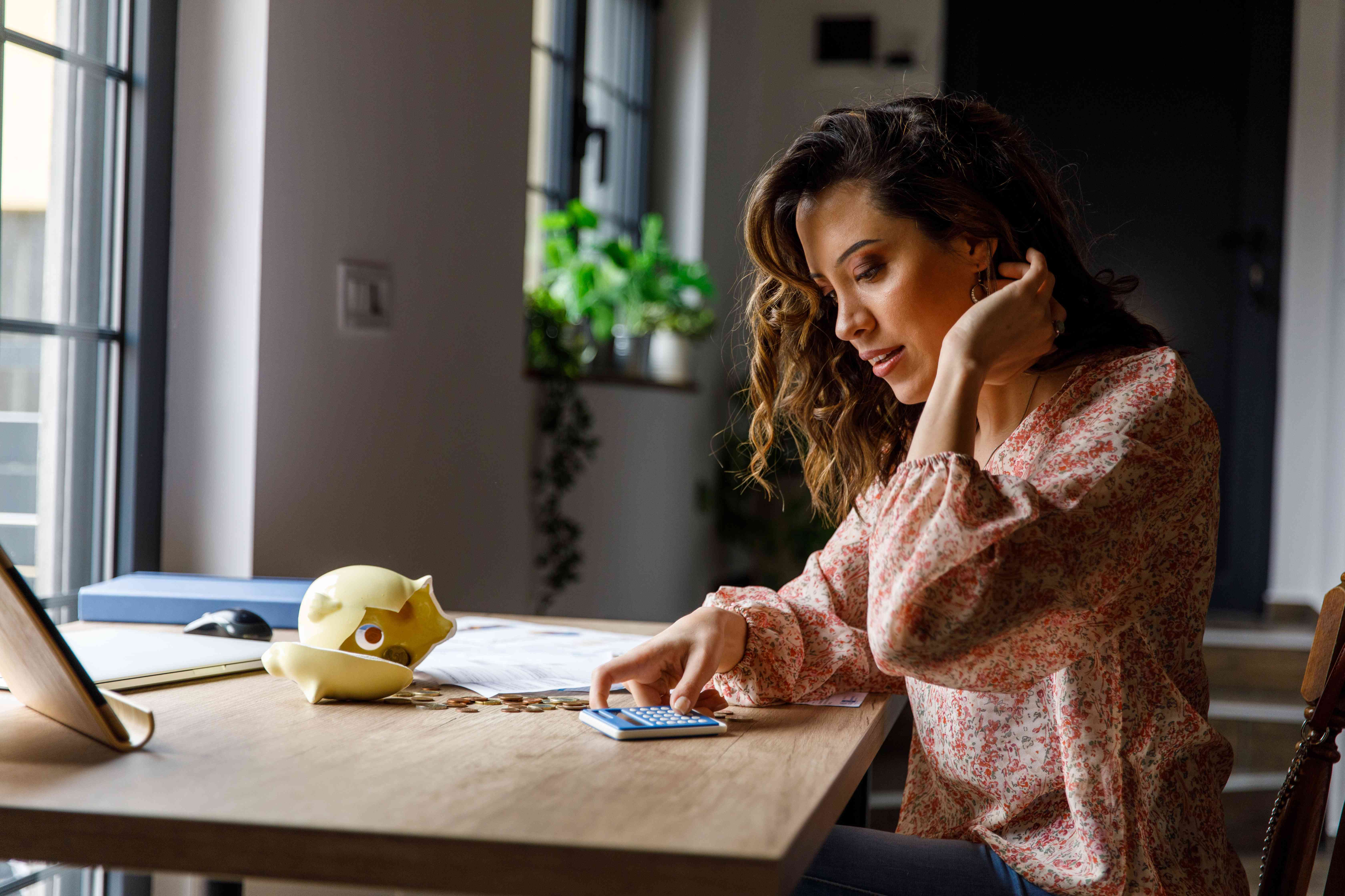 Young woman sitting at home office desk counting her saving from a broken piggy bank