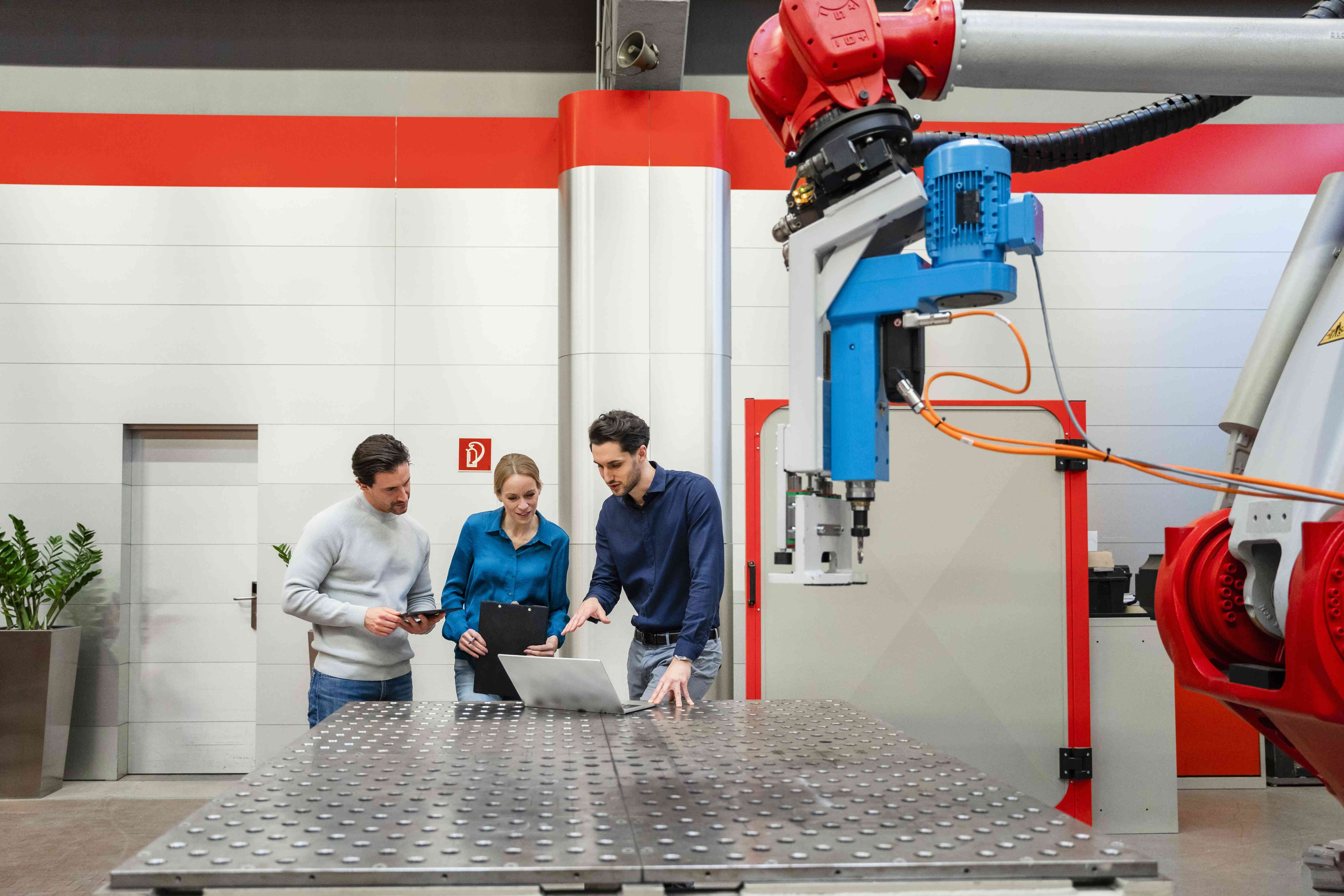 Coworkers in an industrial setting with a robatic arm discussing robot placement in factory